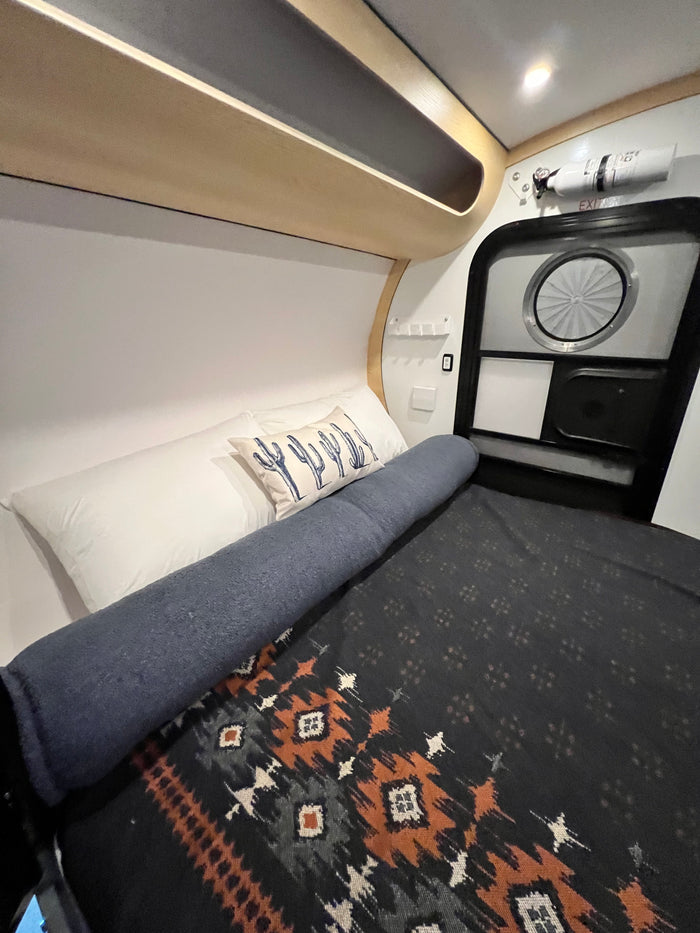 Step inside this cozy RV rental's sleeping area, featuring a Southwestern blanket, cactus pillow, and compact design.