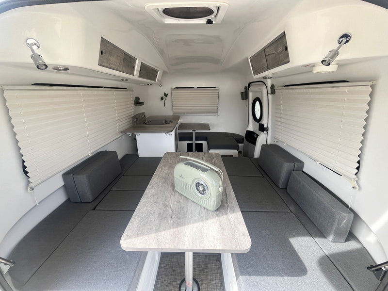 A clean, bright rv rental interior featuring flexible gray cushion seating, a central table, and a small kitchen. — photo 16