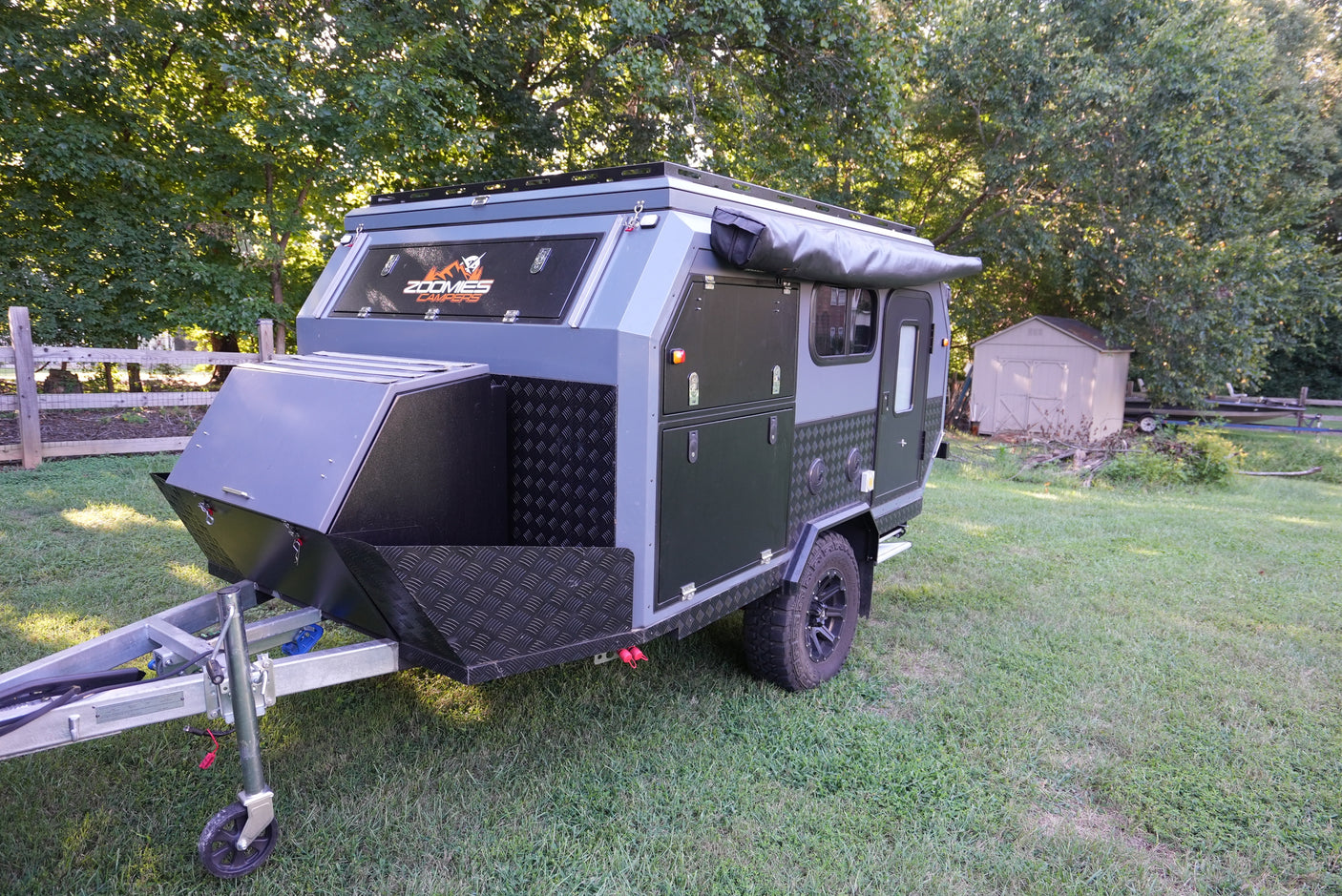 Dark gray and black Zoomies Campers off-road trailer with an awning, perfect for an RV rental adventure, on a grassy lawn.