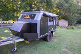 Dark gray and black Zoomies Campers off-road trailer with an awning, perfect for an RV rental adventure, on a grassy lawn.
