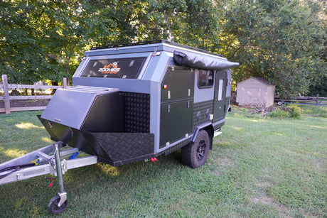 Dark gray and black Zoomies Campers off-road trailer with an awning, perfect for an RV rental adventure, on a grassy lawn.
