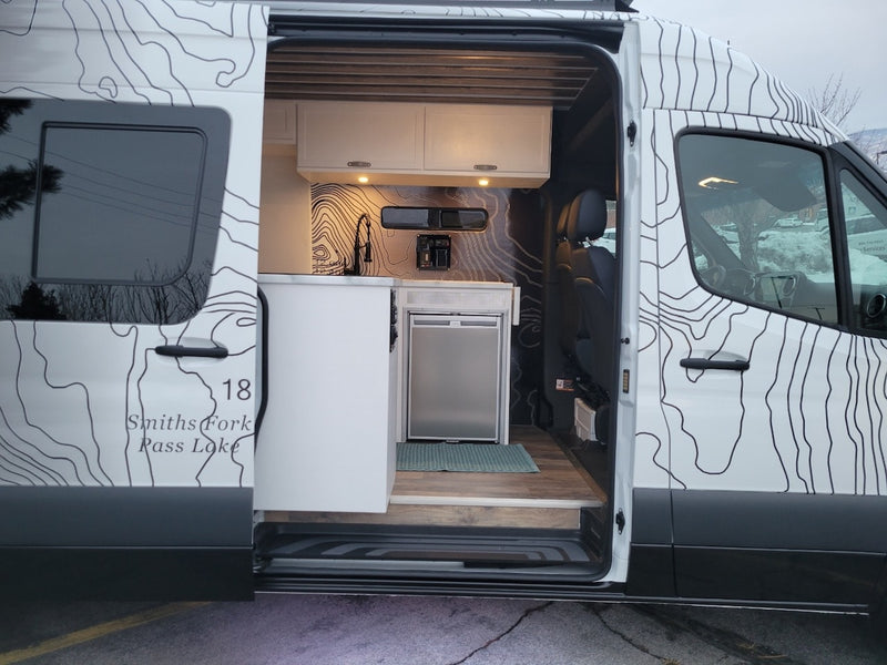 Explore this RV rental's custom camper van interior, featuring a compact kitchen with a sink & fridge. — photo 6