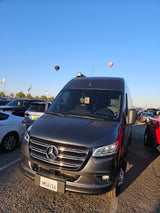 Front view of a dark grey Mercedes-Benz Sprinter RV rental van parked. Two hot air balloons float in the blue sky.