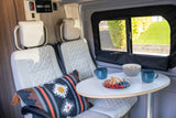 Cozy rv rental interior: comfortable white seating, oval dining table with breakfast (croissants, berries, cereal), and a bright window view.