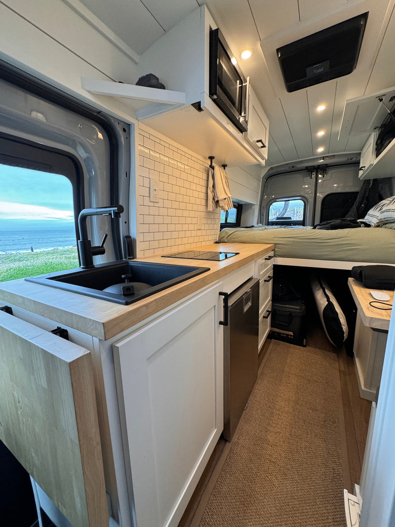 This RV rental boasts a modern kitchen, comfy bed, & ocean views. Compact, bright interior perfect for van life adventures. — photo 4
