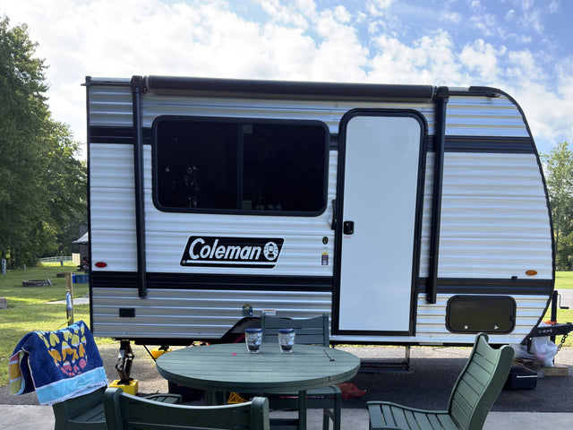 A Coleman travel trailer set up at a sunny campsite with an outdoor table. Perfect for your next rv rental adventure!|Cozy RV rental interior with a comfortable bed