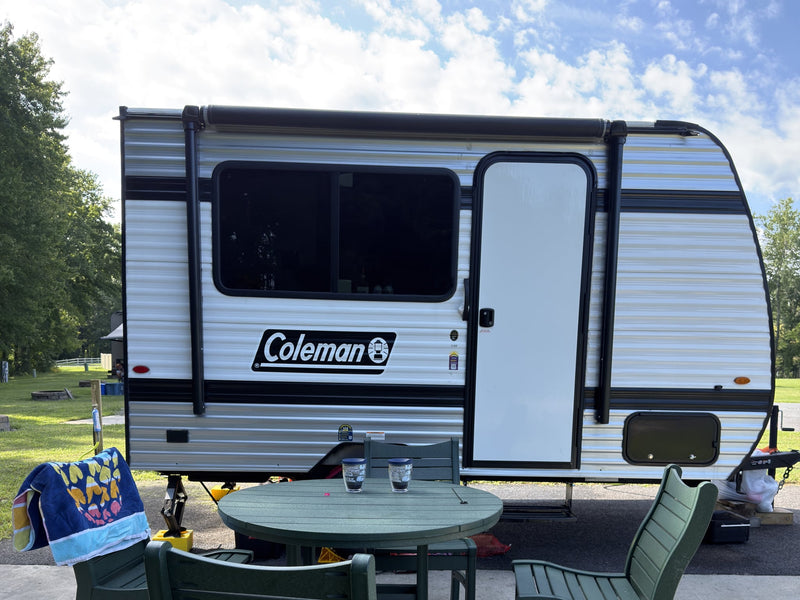 A Coleman travel trailer set up at a sunny campsite with an outdoor table. Perfect for your next rv rental adventure!|Cozy RV rental interior with a comfortable bed — photo 1