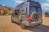 Gray 'REMOTE VANS' adventure RV rental camper van, with off-road tires and roof rack, parked at Red Rocks.