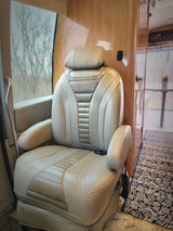 Plush captain's chair in a spacious RV rental. Features light leather, wood paneling, and a window view of trees.
