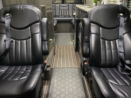 This rv rental features a luxurious van interior with two comfortable black leather captain's chairs, leading to a rear lounge area.