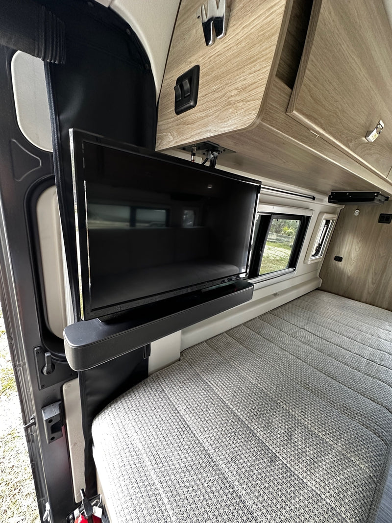 RV rental interior: Mounted TV, patterned bed, and wood storage cabinets in a camper van. — photo 14