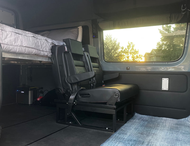 Interior of an RV rental, showing an elevated bed, black leather passenger seats, and a power station, illuminated by window light. — photo 6