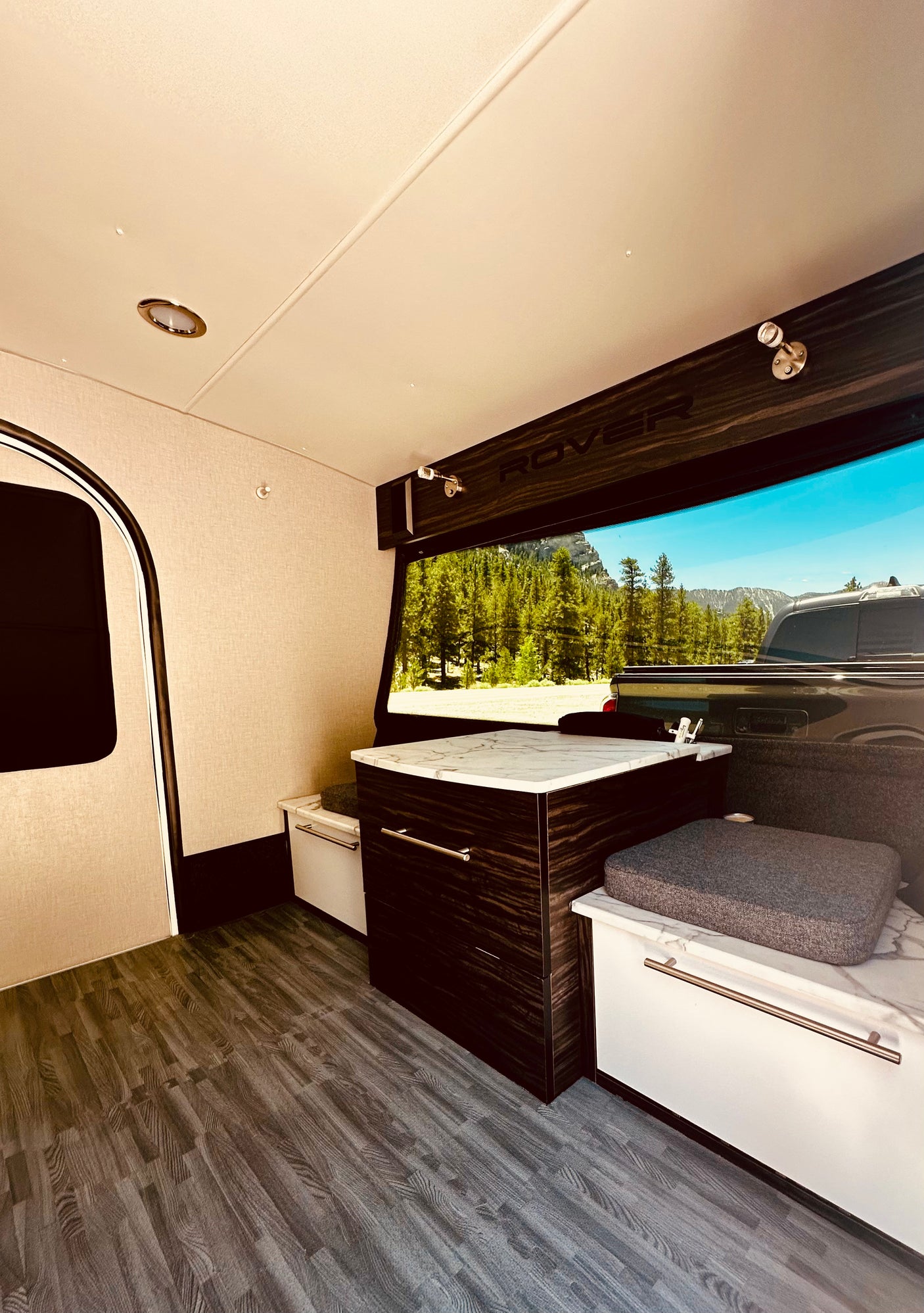Modern RV rental interior featuring a compact kitchenette, comfortable seating, and a wide-open mountain view.