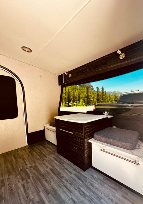 Modern RV rental interior featuring a compact kitchenette, comfortable seating, and a wide-open mountain view.