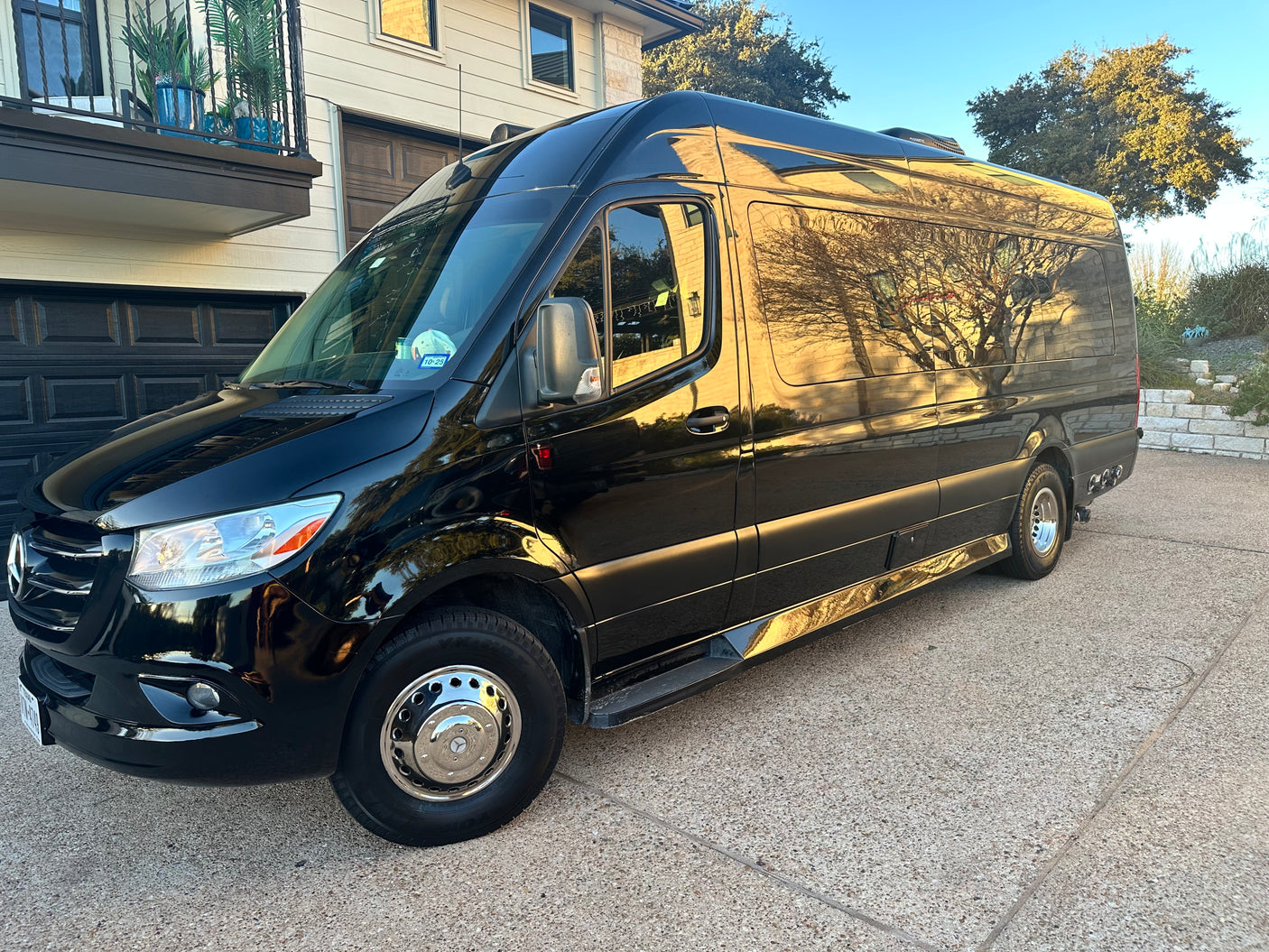 Sleek black Mercedes-Benz Sprinter conversion van, ideal for an RV rental, parked on a sunny driveway.