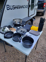 Bushwhacker RV rental kitchen setup: camping pots, pans, kettle, utensils, and tools laid out for outdoor cooking.