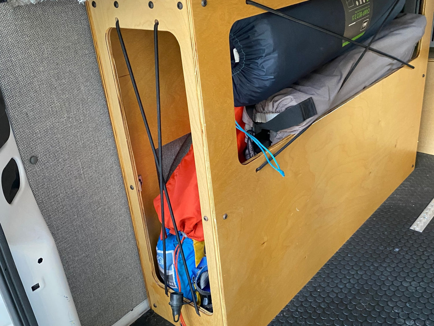 RV rental: Efficient wooden storage in a van conversion, organizing camping gear like sleeping pads with bungee cords. — photo 10