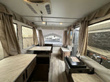 Spacious pop-up RV rental interior with beds, a dinette table, and countertop stove.