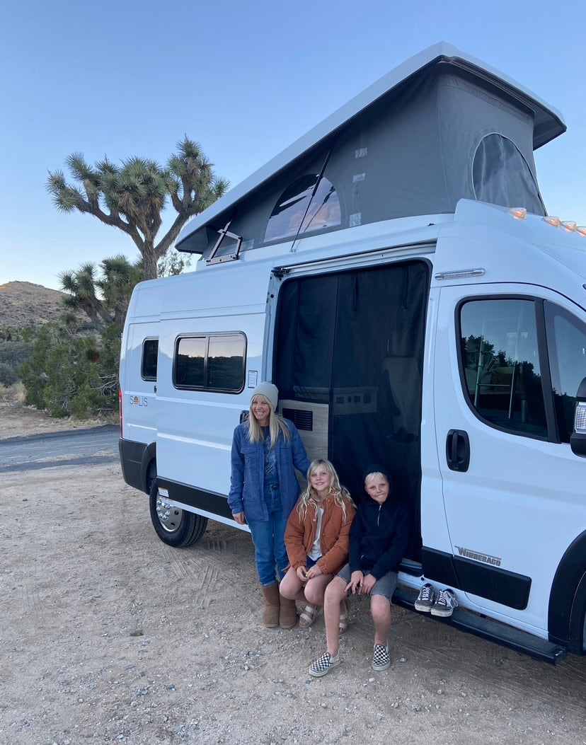  is set up for camping on a gravel lot under a cloudy sky.|Night view of an illuminated white RV rental camper van with its door open — photo 3
