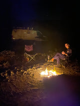 Nighttime rv rental camping scene with a person by a warm campfire. Cozy outdoor adventure.