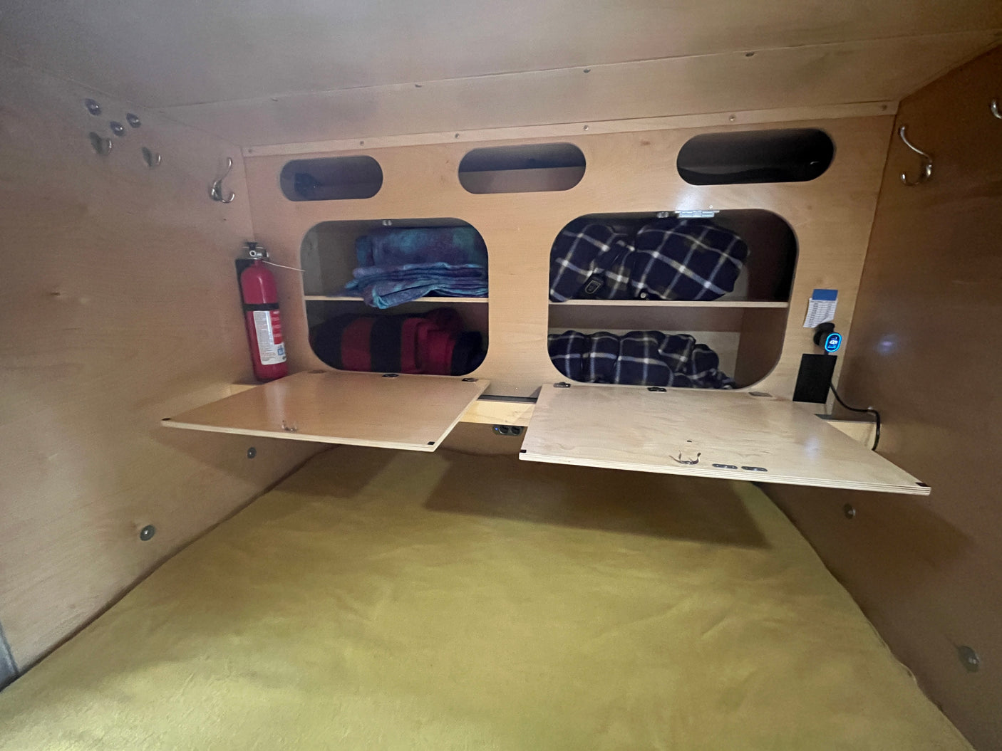 RV rental bedroom view: compact space with overhead storage, blankets, fire extinguisher, and fold-down side tables.