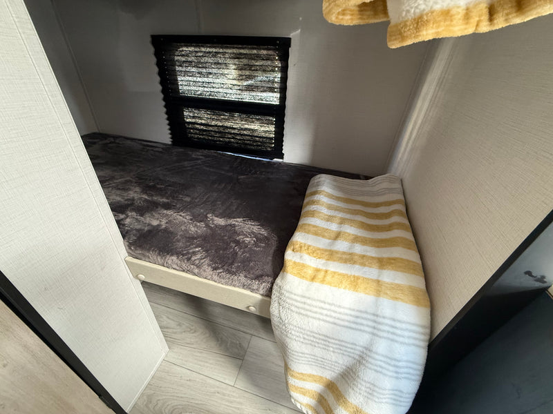 Compact RV rental bunk bed features a grey blanket, striped towel, and window with blinds, creating a cozy sleeping space. — photo 11