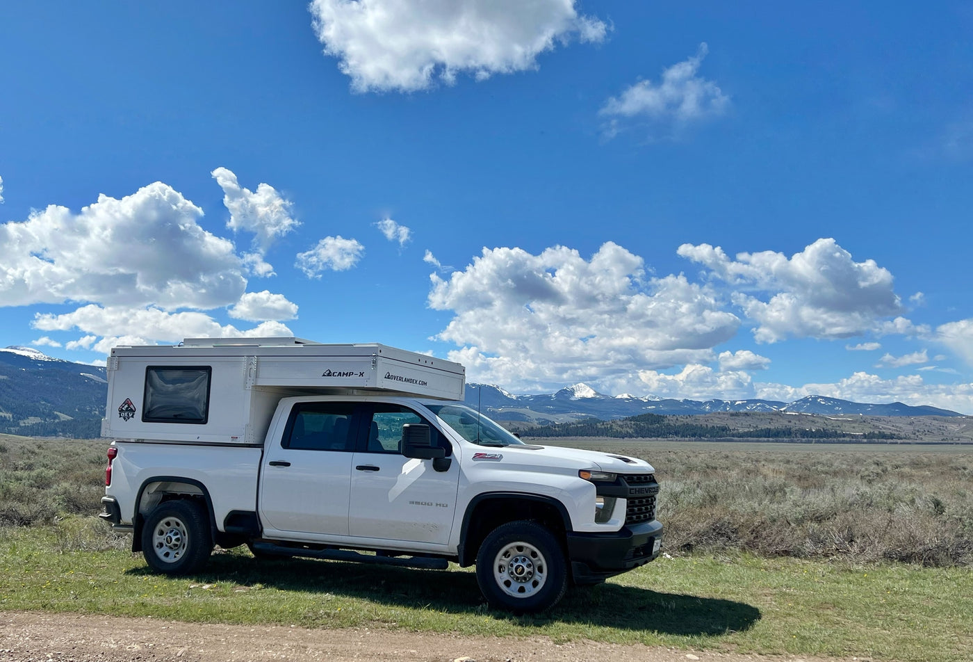 White Chevy truck with a pop-top truck camper, perfect for RV rental trips to scenic mountains under blue skies. — photo 4