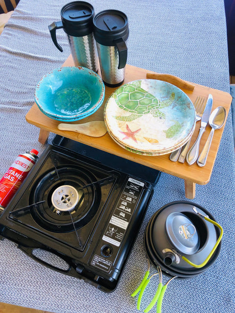Compact outdoor cooking gear for your RV rental adventure: portable stove, kettle, bowls, and plates for easy meals.