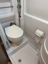 This compact RV rental bathroom features a white toilet, shower with chrome controls, and a toilet paper holder.