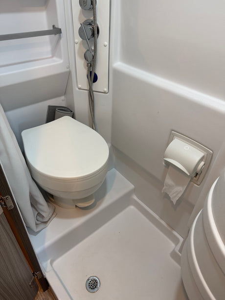 This compact RV rental bathroom features a white toilet, shower with chrome controls, and a toilet paper holder.