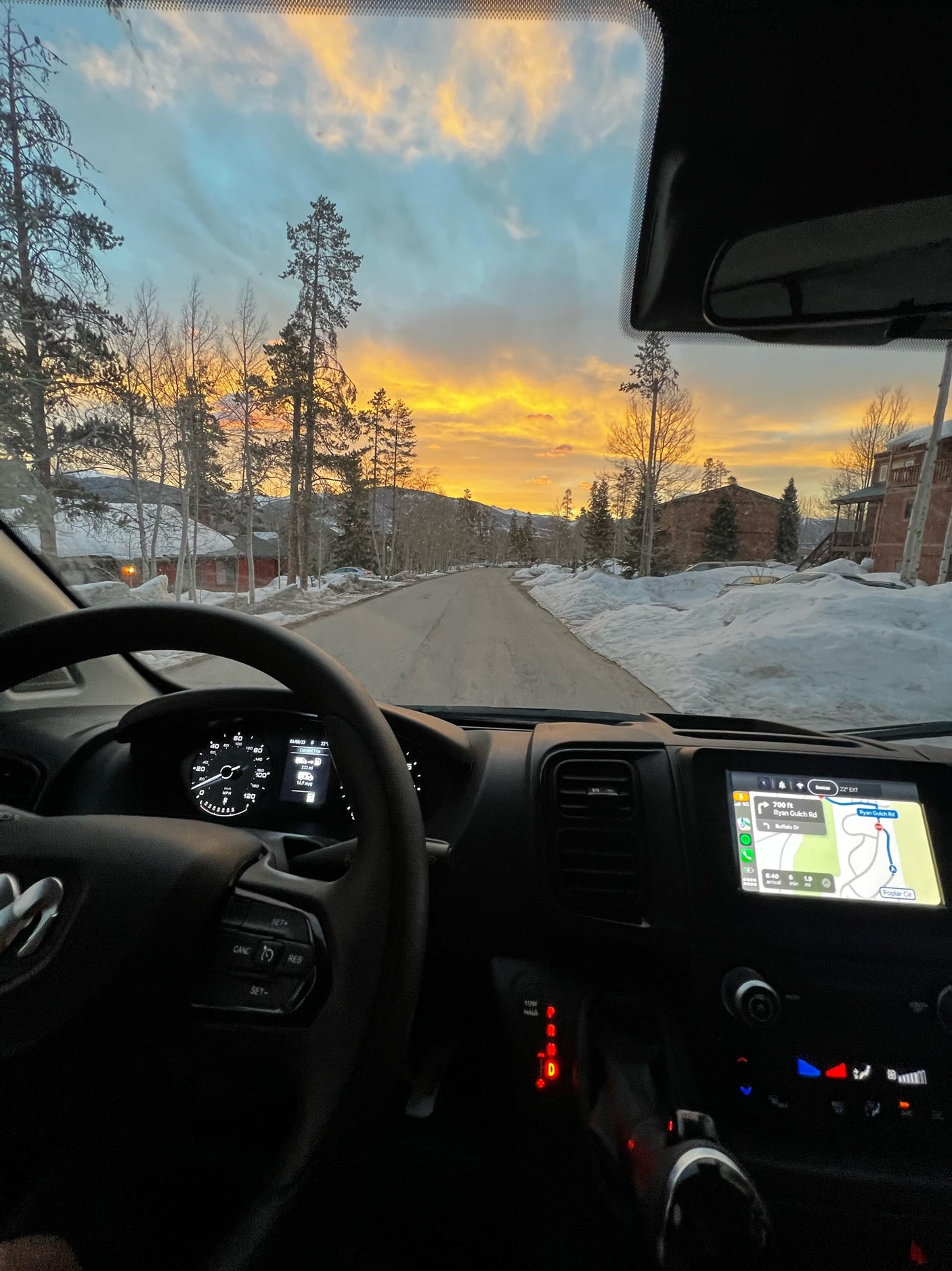 Driver's view from an RV rental at sunrise on a snowy mountain road. Dashboard, navigation to Ryan Gulch Rd, and vibrant sky.