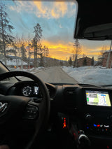 Driver's view from an RV rental at sunrise on a snowy mountain road. Dashboard, navigation to Ryan Gulch Rd, and vibrant sky.