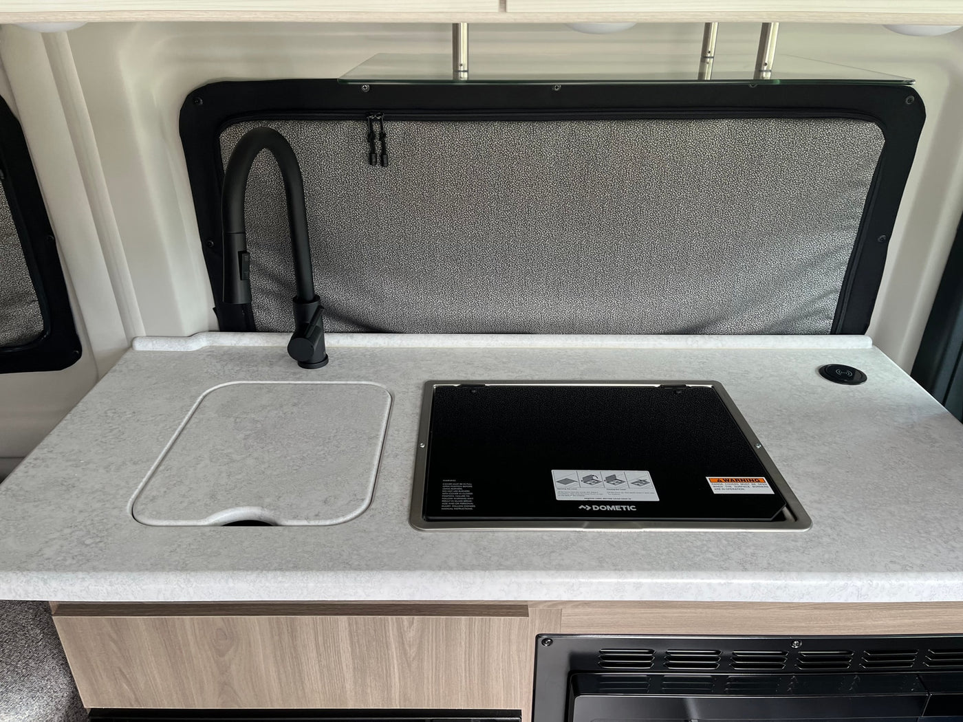 RV rental kitchen: modern counter with sink, black faucet, Dometic stovetop, and wireless charger. — photo 15