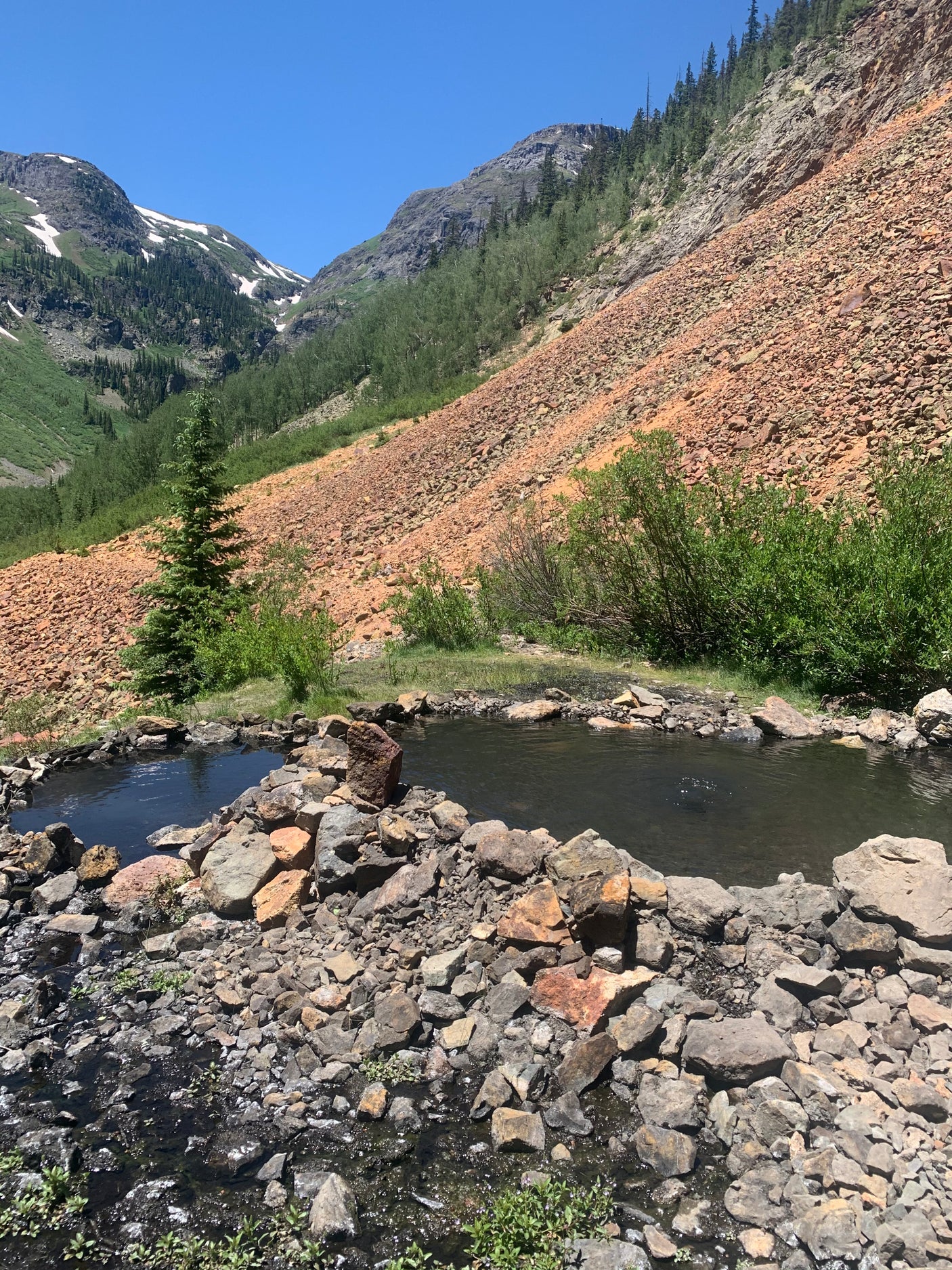 Explore natural hot springs by RV rental. Two small pools in a rocky mountain setting with green slopes and red scree.