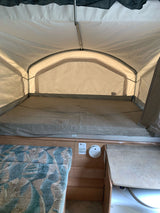 Inside a pop-up RV rental, featuring a spacious bed, light fabric walls, and a small built-in counter area.