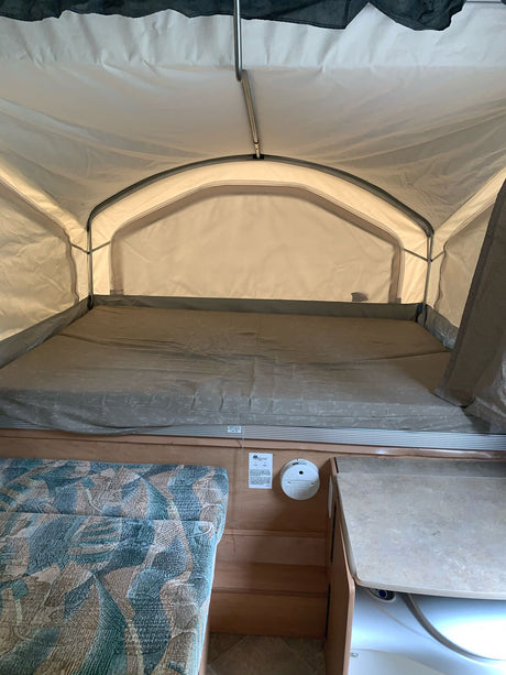 Inside a pop-up RV rental, featuring a spacious bed, light fabric walls, and a small built-in counter area.