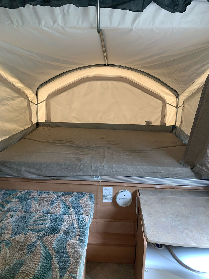Inside a pop-up RV rental, featuring a spacious bed, light fabric walls, and a small built-in counter area. — photo 8