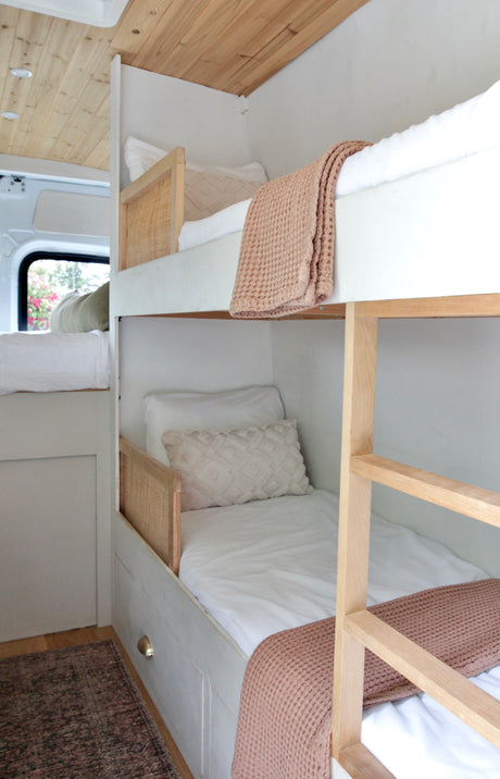 Experience comfort in this RV rental! Custom light wood & rattan bunk beds with soft white bedding, creating a cozy sleeping space.