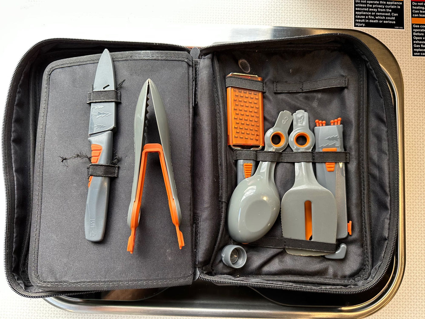 RV rental grilling tools kit: organized knife, tongs, spatula, ladle, and skewers in a compact case for camping cooking.