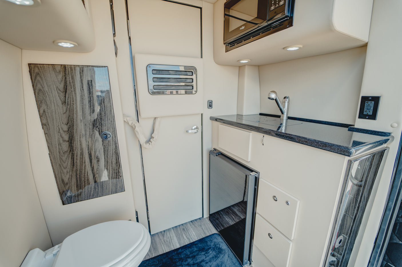 RV rental's compact interior: toilet, kitchenette with sink, microwave, fridge, and wood-paneled door. Bright and functional.