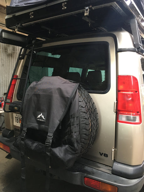 Gold Land Rover Discovery with a roof tent, ladder, & spare tire bag. Ready for adventure, like an RV rental.