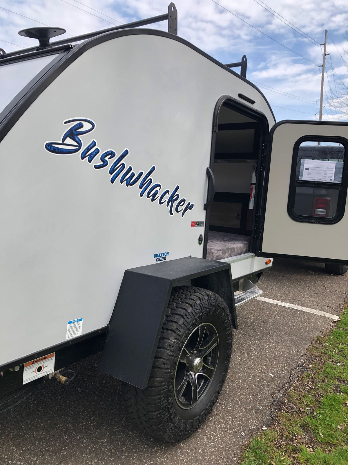 A Bushwhacker teardrop travel trailer for RV rental. Its side door is open, revealing a compact, bed-filled interior. — photo 6
