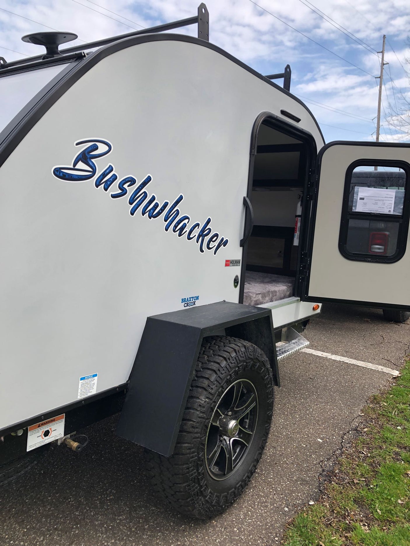 A Bushwhacker teardrop travel trailer for RV rental. Its side door is open, revealing a compact, bed-filled interior.