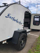 A Bushwhacker teardrop travel trailer for RV rental. Its side door is open, revealing a compact, bed-filled interior.