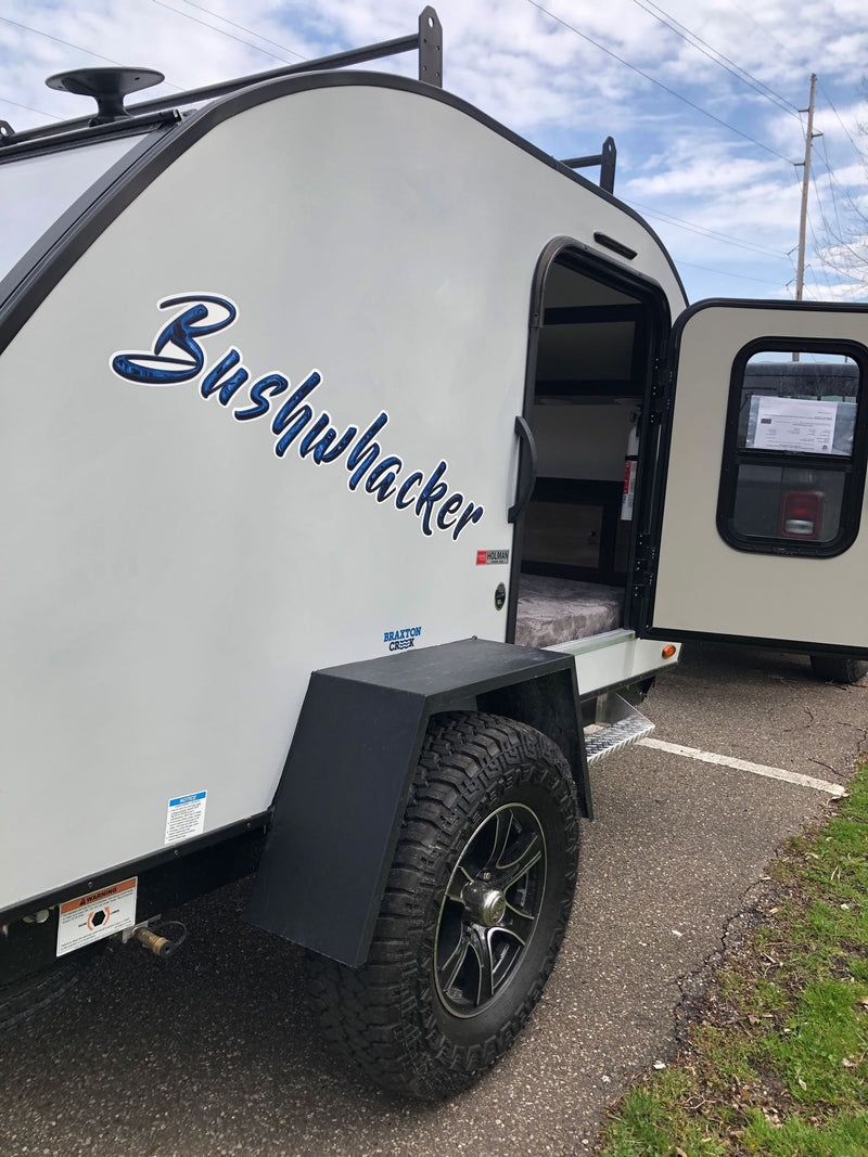 A Bushwhacker teardrop travel trailer for RV rental. Its side door is open, revealing a compact, bed-filled interior. — photo 6