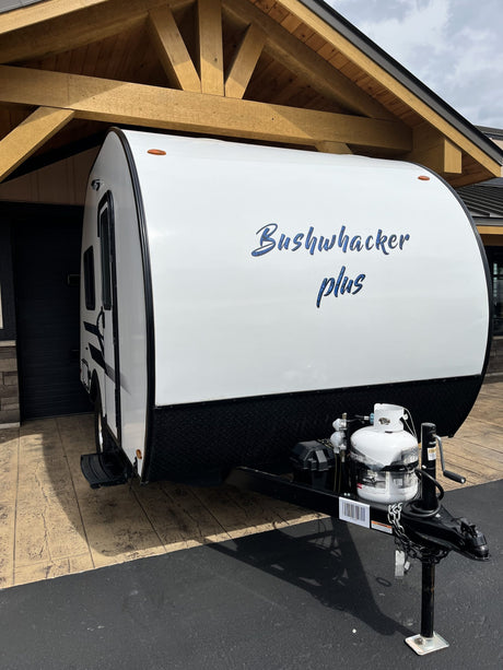 A white Bushwhacker plus travel trailer, with a propane tank at the front, is ready for an RV rental.