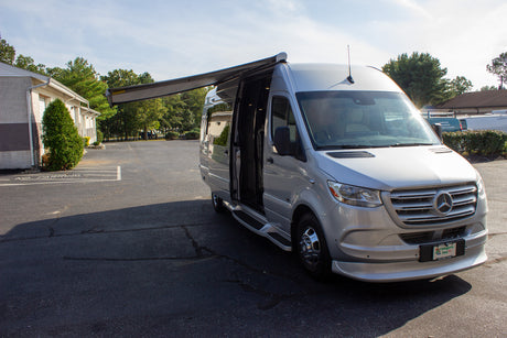 Silver Mercedes-Benz Sprinter RV rental van with an extended awning, parked on asphalt.