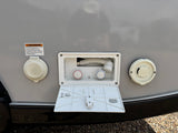 An RV rental's side panel featuring a 30-amp electrical inlet, an outdoor shower, and a water fill port. Essential camping utilities.