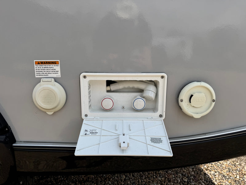 An RV rental's side panel featuring a 30-amp electrical inlet, an outdoor shower, and a water fill port. Essential camping utilities. — photo 6