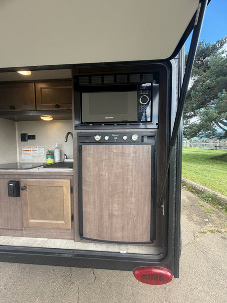 RV rental outdoor kitchen: microwave, fridge, sink, and cabinets, with a scenic lake and tree view.